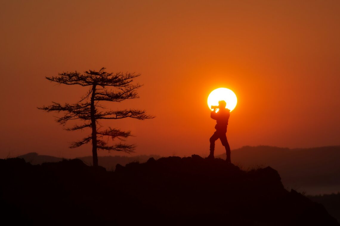 A person standing on top of a hill with the sun in the background