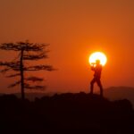 A person standing on top of a hill with the sun in the background