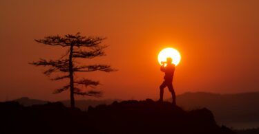 A person standing on top of a hill with the sun in the background