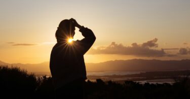 A man standing on top of a hill looking at the sun