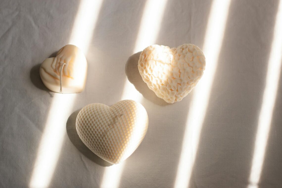 Three heart-shaped candles with textured designs basking in soft sunlight on a minimalist surface.