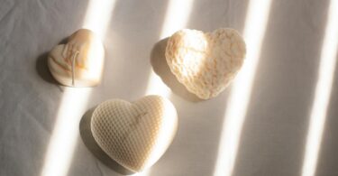 Three heart-shaped candles with textured designs basking in soft sunlight on a minimalist surface.